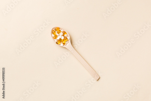 Vitamin capsules in a wooden spoon on a colored background. Pills served as a healthy meal. Drugs, pharmacy, medicine or medical healthycare concept