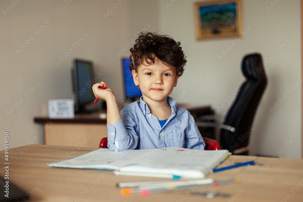 Preschool education online. A cheerful and energetic preschooler at the computer is engaged, next to notebooks, pencils. Lesson with a teacher remotely. Preschool education online. A cheerful and energetic preschooler at the computer is engaged, next to notebooks, pencils. Lesson with a teacher remotely.