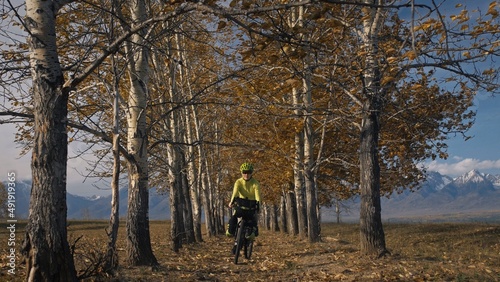 The woman travel on mixed terrain cycle touring with bikepacking. The traveler journey with bicycle bags. Sportswear in green black colors. The trip in magical autumn forest, arch, alley, avenue. © ivandanru