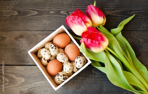 Decorative Easter card.  On a wooden brown background lies a white wooden box with Easter eggs  early spring flowers tulips.  Flat lay  close-up.  Easter bright holiday concept.