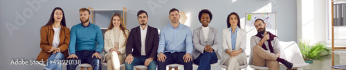 Diverse team of business people sitting in office. Group of happy company employees attending staff training meeting, lecture, workshop or seminar, sitting in row and looking at camera. Banner, header © Studio Romantic