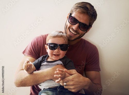 Coolness runs in this family. A young father and his infant son wearing matching sunglasses and laughing. photo