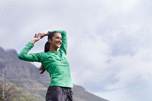 Enjoying the view from the top. A young ethnic woman stretching while looking at the views from the mountain peak.
