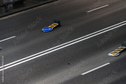 A road sign with a white arrow on a blue background lies on the roadway. A strong wind knocked over a road sign.