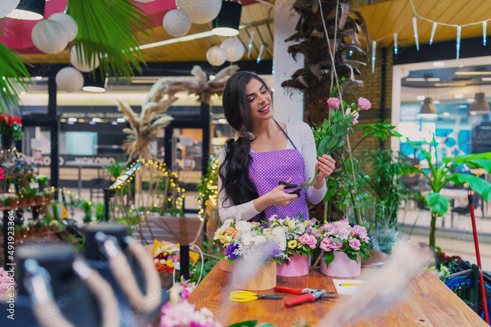 Beautiful florist stands behind a counter in a flower shop and makes a bouquet using garden scissors