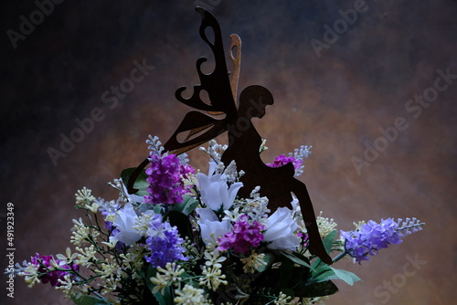 a little fairy perched on top of a bouquet of colorful flowers and brown background