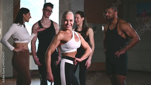 Group of happy smiling muscular sports fitness female and male adults people standing together as good friends in gym with sport equipment in background after a difficult workout session