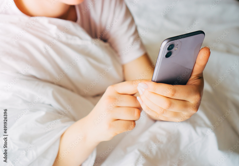 A close-up of a woman's hands holding a smartphone, a woman woke up lying in bed and started the day with an online viewing of a website. A close-up of a woman's hands holding a smartphone, a woman woke up lying in bed and started the day with an online viewing of a website.