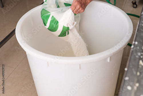 older man's hands pouring salt into plastic container to prepare brine