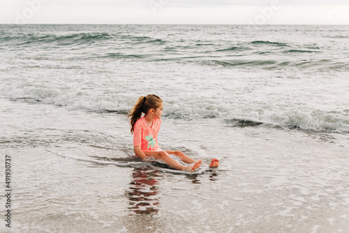 Young girl sits in the ocean looking out at Kure Beach photo