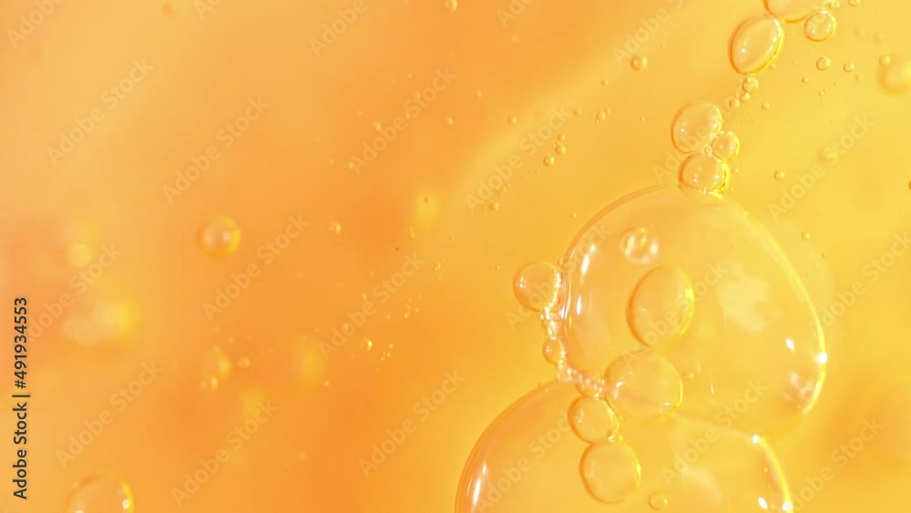 Vitamin C serum texture with dropper and slowly moving bubbles, orange cosmetics gel, macro shot.
