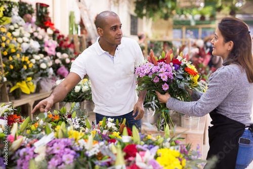 Experienced woman florist helping male client to choose flowers in flower shop © JackF
