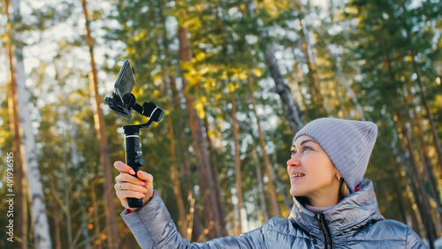 Woman Holding On Handheld Film 3-axis Gimbal Stabilization Device in Winter for Smartphone. Girl Blogger Make Selfie, Broadcast Video Blogging, Vlogging. Videographer Operator Take Photo Video.
