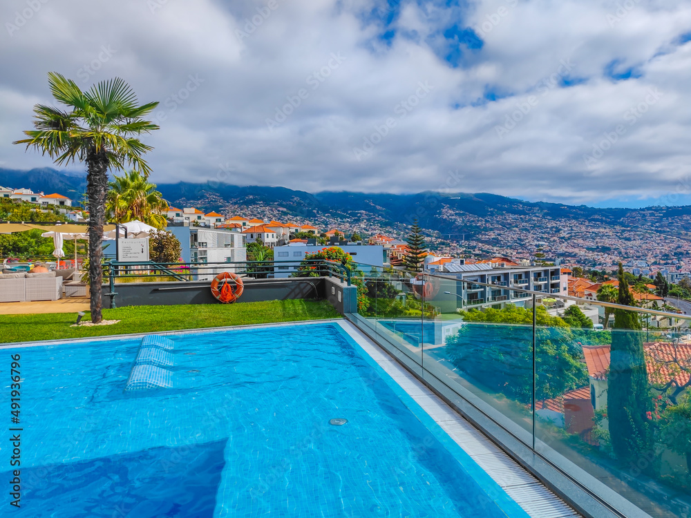 Panoramic view pool with sunbeds in water, located on a mountain with a view to Funchal, capital of Madeira island