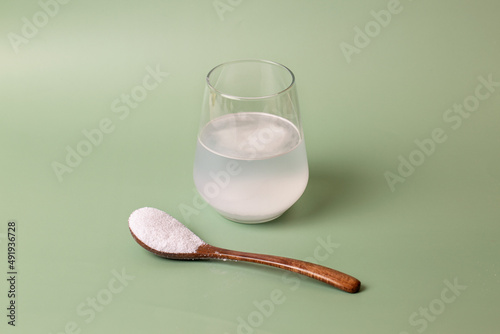 Foto White collagen powder in a transparent glass with water and a wooden spoon on a green background