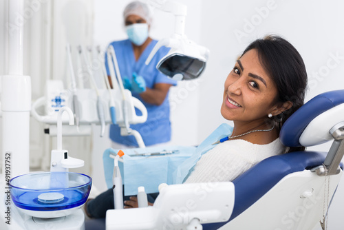 Happy woman sitting in dental chair after teeth cure giving thumb up