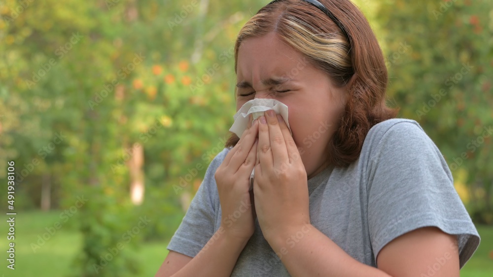 A young girl with allergies in an autumn park. Sneezing girl blows her nose into a napkin and sneezes. selective focus A young girl with allergies in an autumn park. Sneezing girl blows her nose into a napkin and sneezes. selective focus