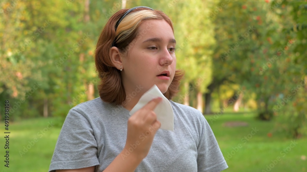 A young girl with allergies in an autumn park. Sneezing girl blows her nose into a napkin and sneezes. selective focus A young girl with allergies in an autumn park. Sneezing girl blows her nose into a napkin and sneezes. selective focus