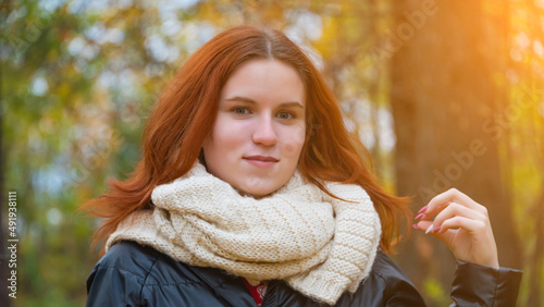 portrait of a red-haired smiling girl in a jacket and scarf straightening her hair against the background of autumn nature and the bright sun the concept of human emotion