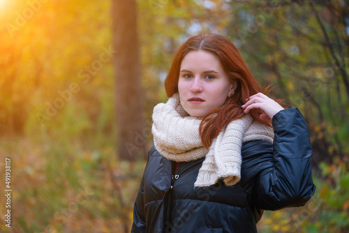 portrait of a red-haired smiling girl in a jacket and scarf straightening her hair against the background of autumn nature and the bright sun the concept of human emotion
