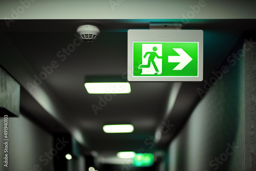 Green fire exit sign on hallway aside of smoke alarm device Fototapeta