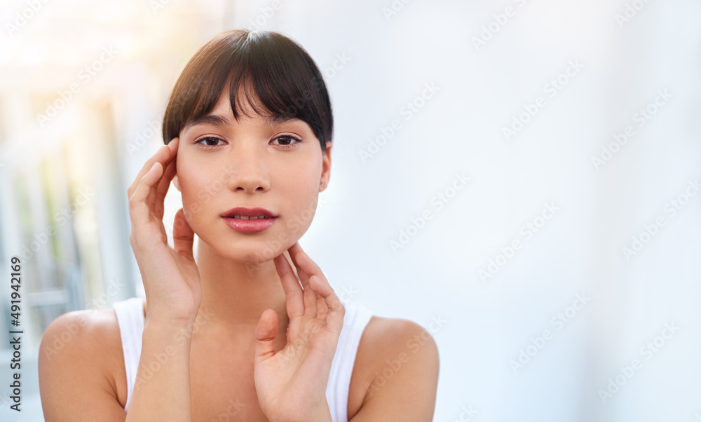 Radiant and beautiful. Portrait of a cheerful attractive young woman touching her face while looking into a mirror at home during the day. Radiant and beautiful. Portrait of a cheerful attractive young woman touching her face while looking into a mirror at home during the day.
