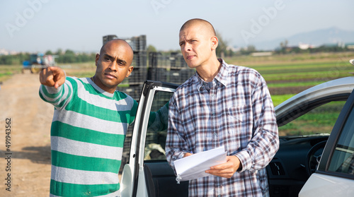 Farmers signing papers and communicating near car on the farmer field