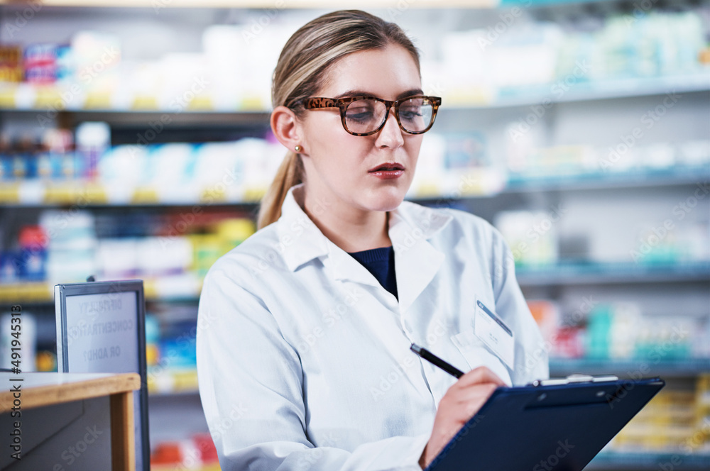 Taking notes of all the medical stock in store. Shot of a young pharmacist writing on a clipboard in a pharmacy. Taking notes of all the medical stock in store. Shot of a young pharmacist writing on a clipboard in a pharmacy.