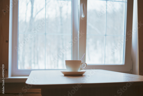 A cup on the table in front of the window.