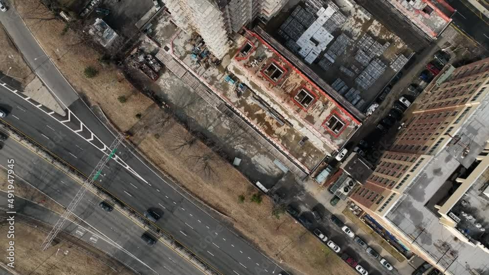 A high angle view above Shore Parkway in Brooklyn, NY. The drone camera tilt straight down, dolly in and rotate and boom up high over a high-rise construction site on a cloudy day.