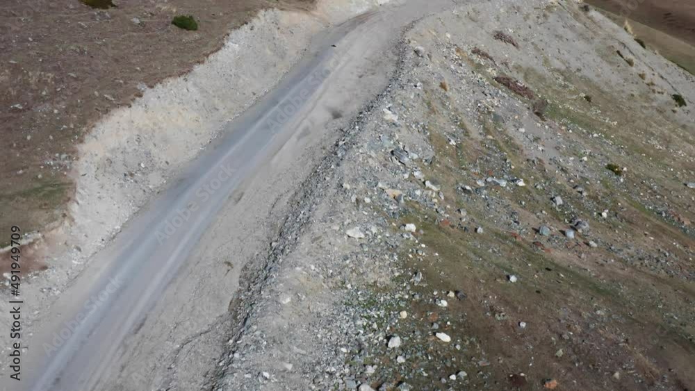 Top view of a flight over a sandy mountain road with a lot of stones and green grass. Flying a drone over a mountain village road on a sunny day with the shadow of a copter. A road with crushed stone. Top view of a flight over a sandy mountain road with a lot of stones and green grass. Flying a drone over a mountain village road on a sunny day with the shadow of a copter. A road with crushed stone.