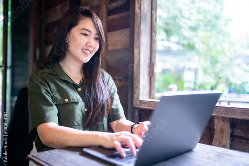 Happy of asian freelance people business female  wearing brownish green dress stylish hipster casual working with laptop computer with coffee cup beside the window of a wooden house background © Thinapob