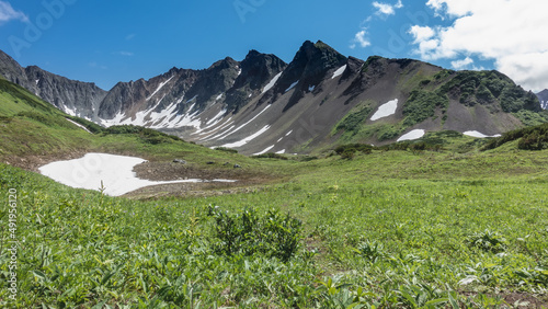 A picturesque crater of an extinct volcano against a blue sky. Snow on the slopes. There is green vegetation in the valley. Kamchatka. Vachkazhets 