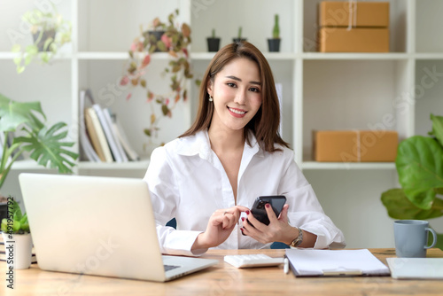 Charming Asian woman with a smile sitting holding smartphone at the office.