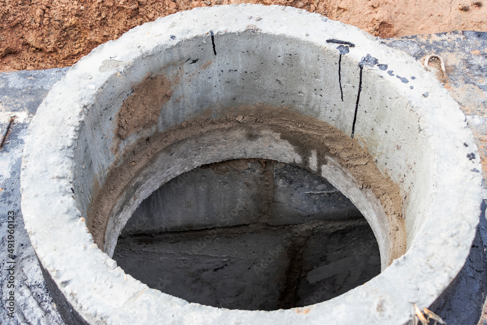 Installation of a reinforced concrete well for water supply and sewerage at the construction site. Well rings with cast iron hatch and construction tool.