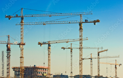 Viele Baukräne auf einer Großbaustelle mit einem Rohbau vor wolkenlosem Himmel photo