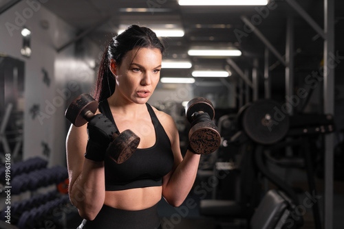 Training in the gym by a beautiful woman in black clothes she uses a dumbbell. Sports girl warms up before training lifts dumbbells. © mtrlin