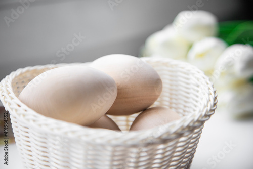 White Easter eggs in a close-up basket, with white tulips lying nearby. Holiday concept