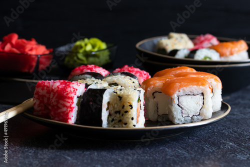 Sushi rolls lie on black plates on dark background, side view, horizontal