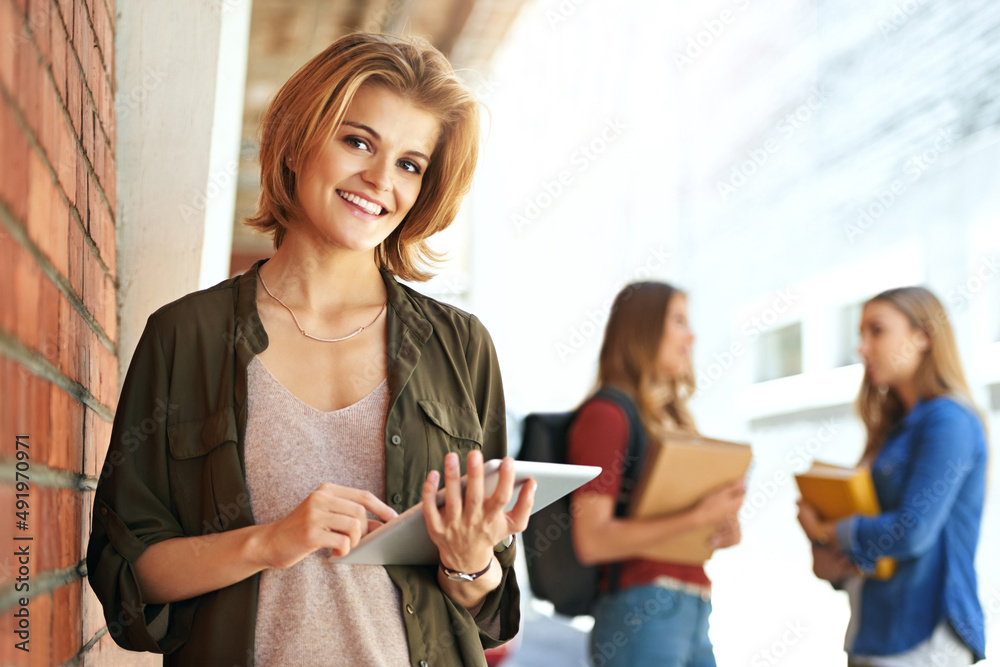Technology is helping me excel at college. Portrait of a smiling female university student standing on campus using a digital tablet with friends in the background. Technology is helping me excel at college. Portrait of a smiling female university student standing on campus using a digital tablet with friends in the background.