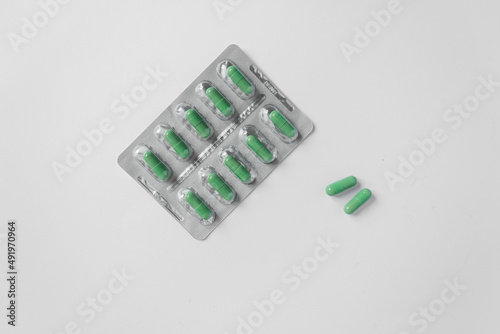 Silver blister with supplements and vitamins in green capsules on white background. Health care concept. Top view.