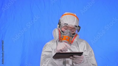Scientist virologist in respirator makes write in an tablet computer with stylus. Woman wearing protective medical mask. Concept health safety virus coronavirus epidemic 2019 nCoV. Chroma key blue. photo