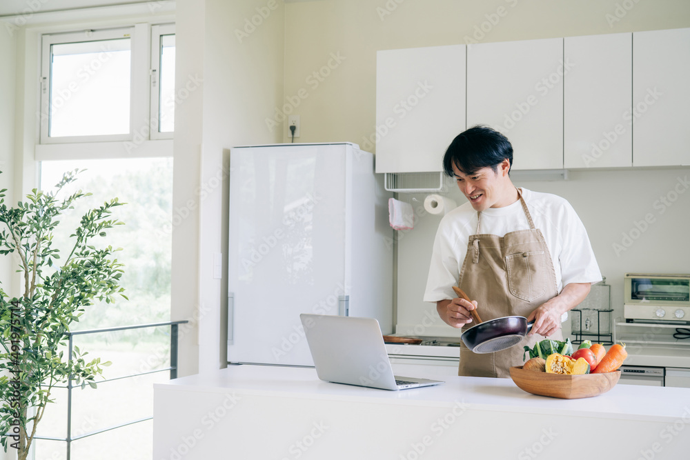 パソコンを見ながら料理する男性(笑顔)
パソコンを見ながら料理する男性(笑顔)