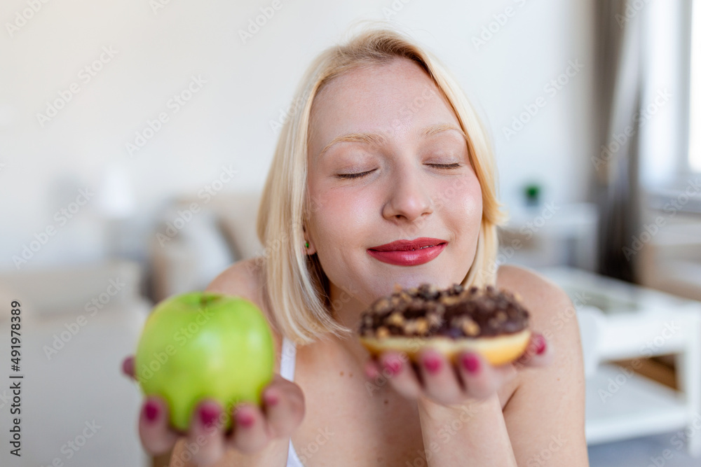 What to choose Healthy or unhealthy. Portrait of a beautiful young woman choosing between an apple or a donut What to choose Healthy or unhealthy. Portrait of a beautiful young woman choosing between an apple or a donut