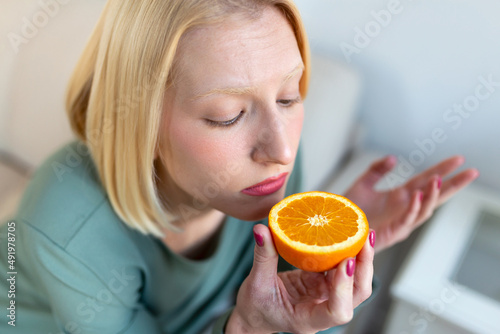 Sick woman trying to sense smell of half fresh orange, has symptoms of Covid-19, corona virus infection - loss of smell and taste. One of the main signs of the disease. photo