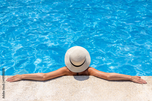 Femme au chapeau qui se détend dans l'eau au bord d'une piscine
