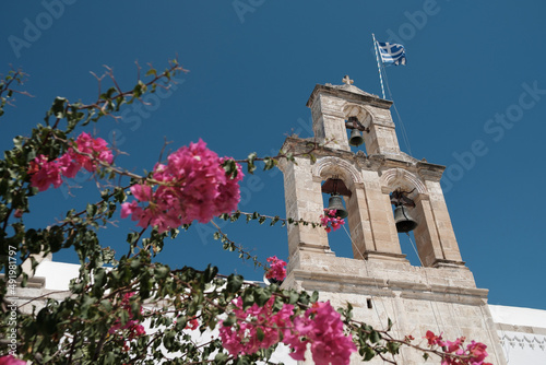 Stara wieża z dzwonami powiewająca grecka flaga niebieskie niebo i różowy kwiat na pierwszym planie