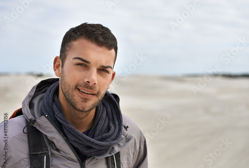 No climate is too much. Portrait of a young male hiker walking along the sand dunes.