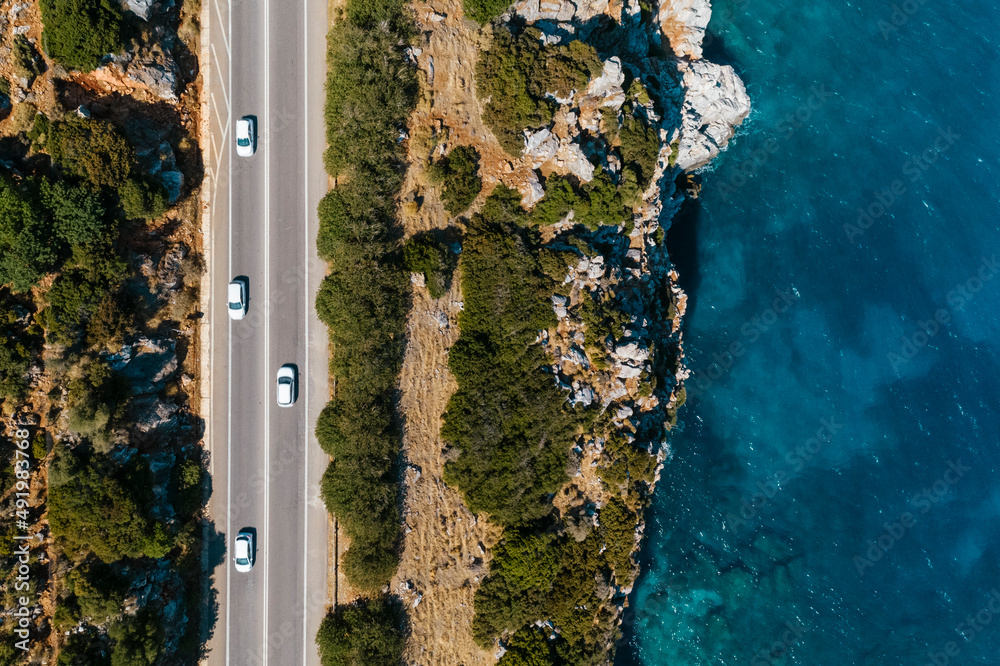 Ujęcie z drona na malowniczo położoną drogę przy stromym wybrzeżu morza śródziemnego na wyspie Kreta w Grecji, turkusowa woda, skały i zielona roślinność, samochody - obrazy, fototapety, plakaty 