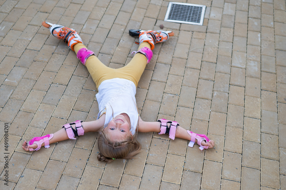 Naklejka premium Little girl learns to roller skate and falls. View from above